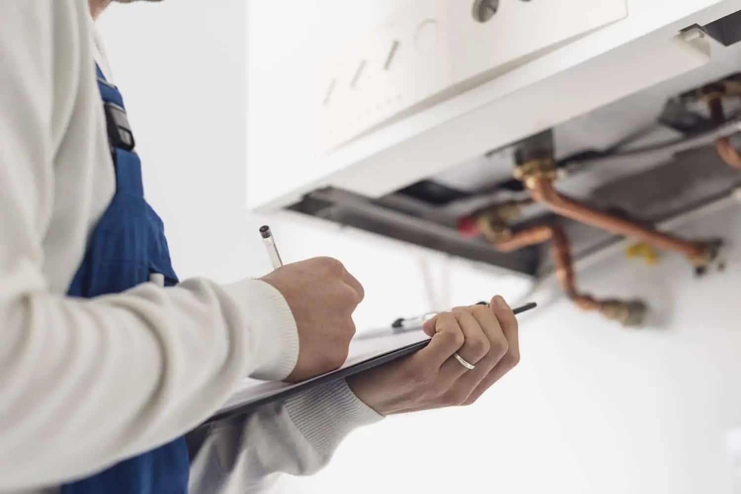 HVAC technician standing in front of a boiler with a clipboard 